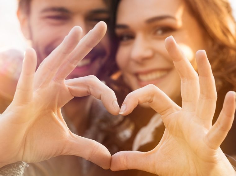 A happy couple making a heart shape with their hands.