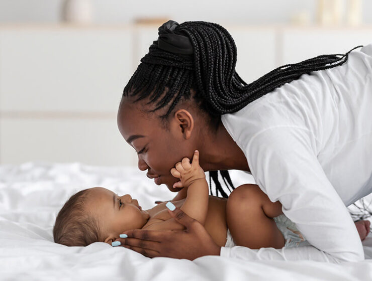 Young mother leans over her baby on a bed