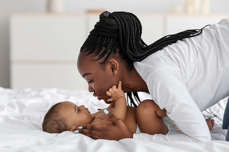 Young mother leans over her baby on a bed